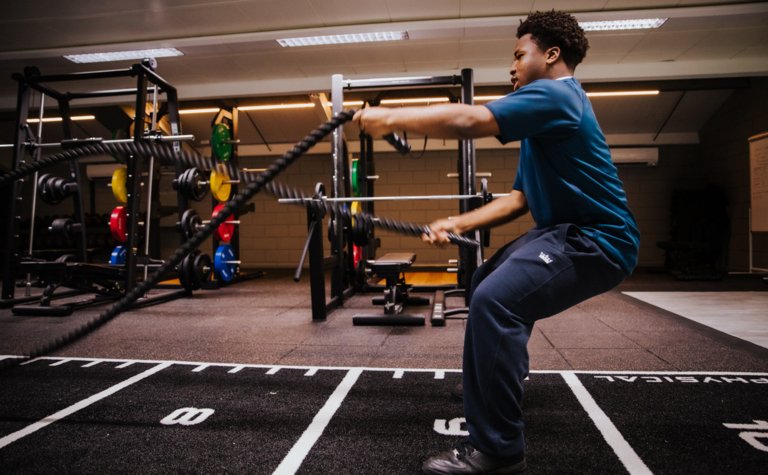Teenage boy using battle ropes in a gym