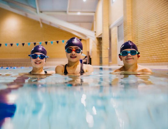 2 boys and a girl smiling stood in an indoor swimming pool